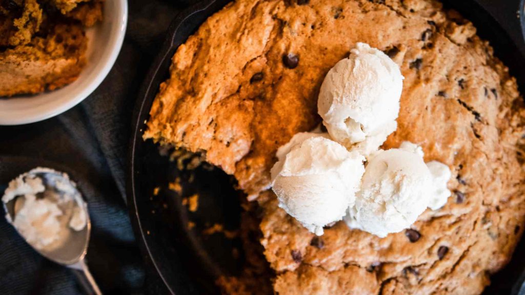 sourdough pumpkin chocolate chip skillet cookie with one scoop out of it and ice cream on top