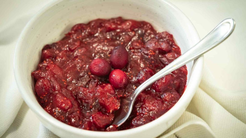 close up of a bowl of cranberry sauce with orange juice and honey with a spoon and whole cranberries on top
