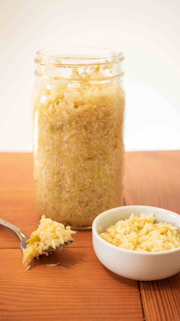 mason jar of lacto-fermented sauerkraut with small bowl of sauerkraut in front of it with a forkful of sauerkraut