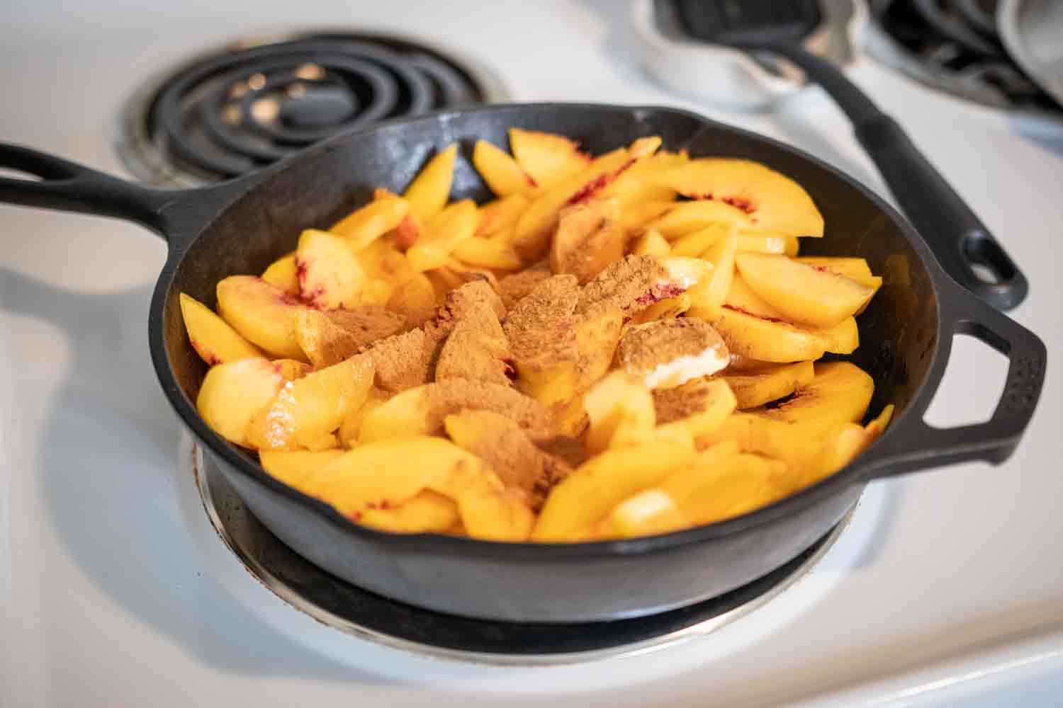 cast iron skillet of peaches cooking down with butter, maple syrup and cinnamon
