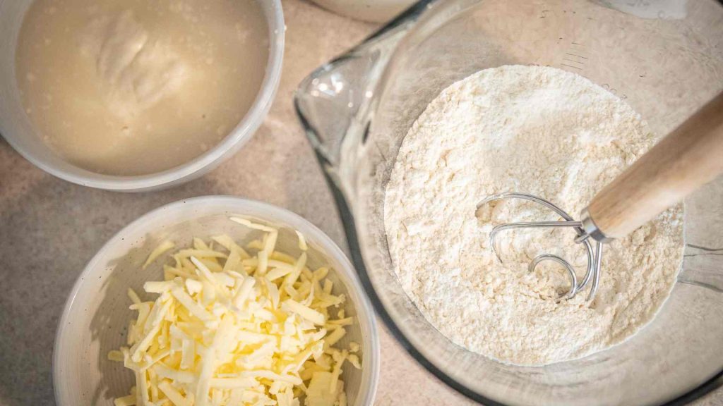 dry ingredients in a bowl with a dough whisk with shredded butter and wet ingredients