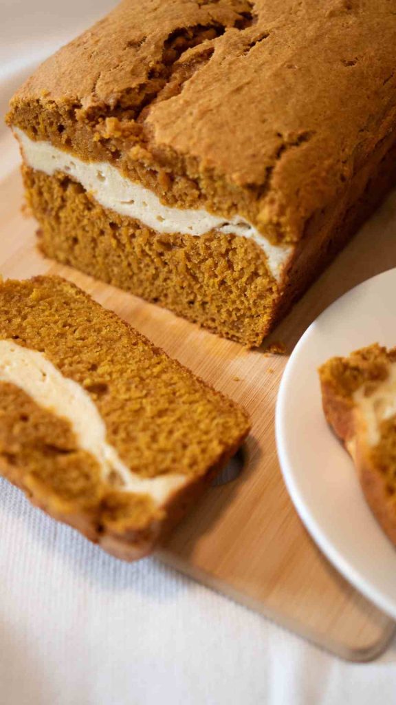 pumpkin sourdough bread loaf with one piece cut off the end. A beautiful deep orange bread with a cream cheese layer in the middle