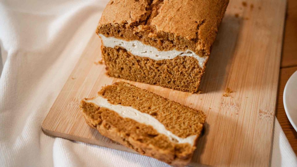 pumpkin sourdough bread loaf with one piece cut off the end. A beautiful deep orange bread with a cream cheese layer in the middle