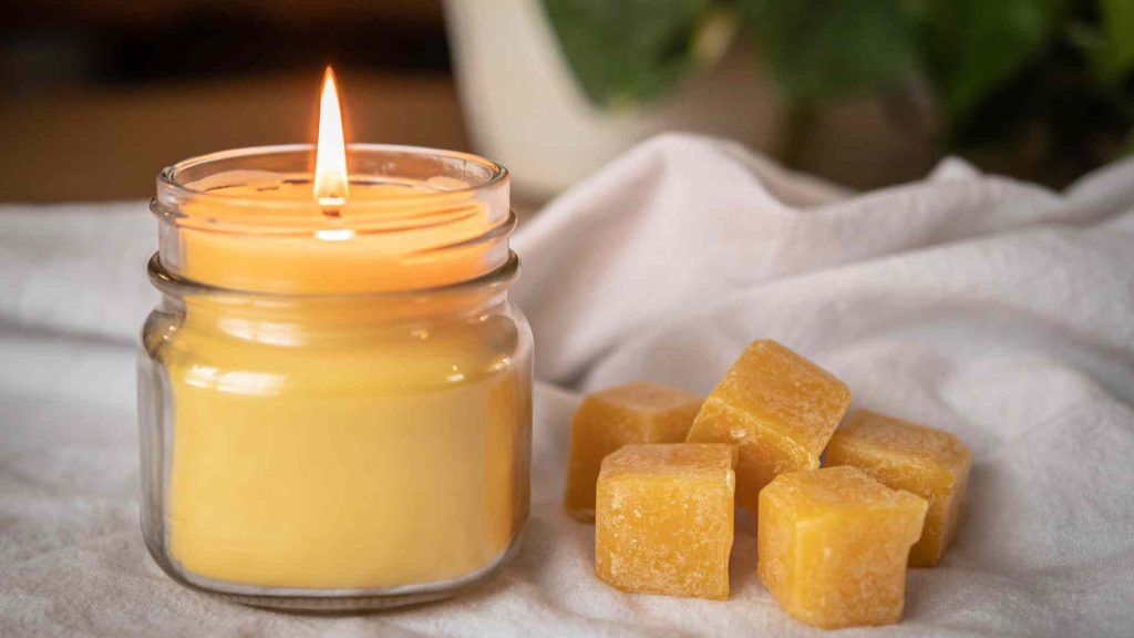 beeswax candle burning on a white background with cubes of beeswax next to it