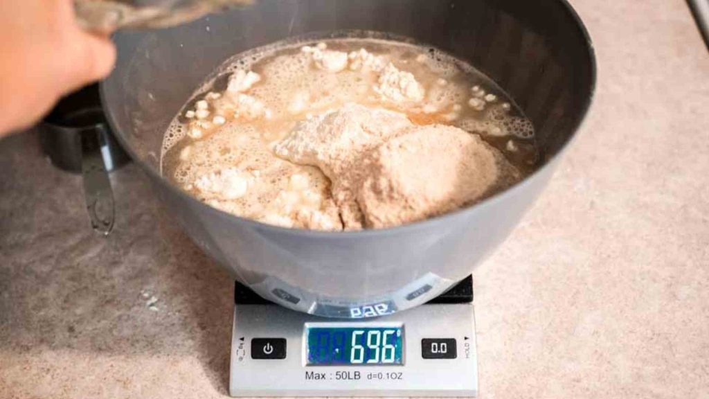 a bowl on a kitchen scale shown weighing all of the ingredients for dutch oven sourdough bread in a bowl