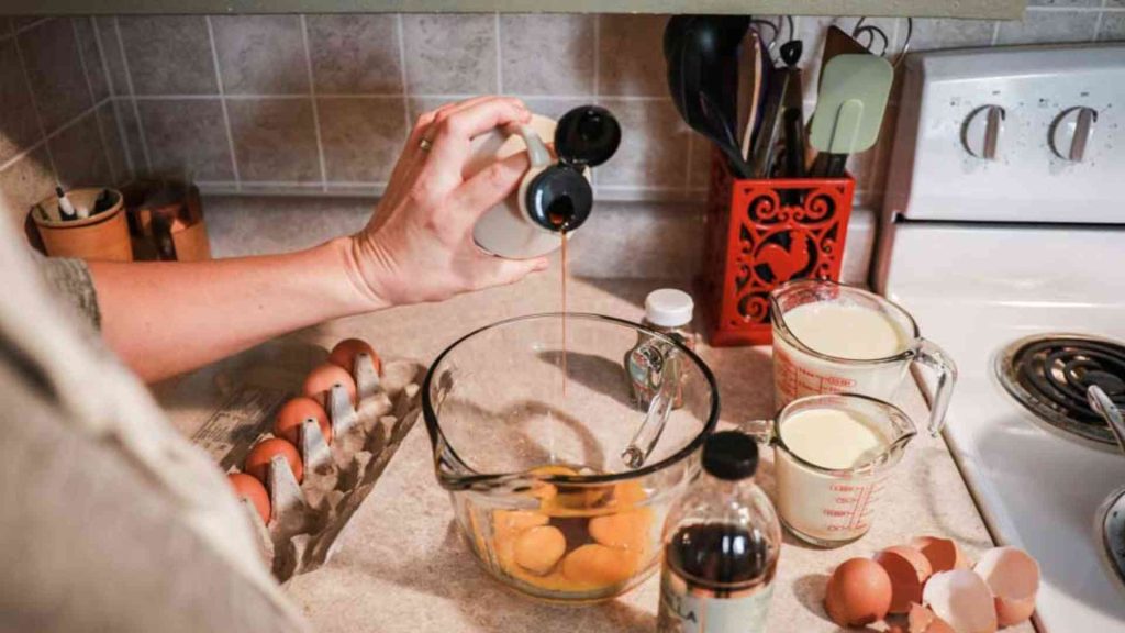 maple syrup being poured into the bowl of egg whites with various ingredients in the background