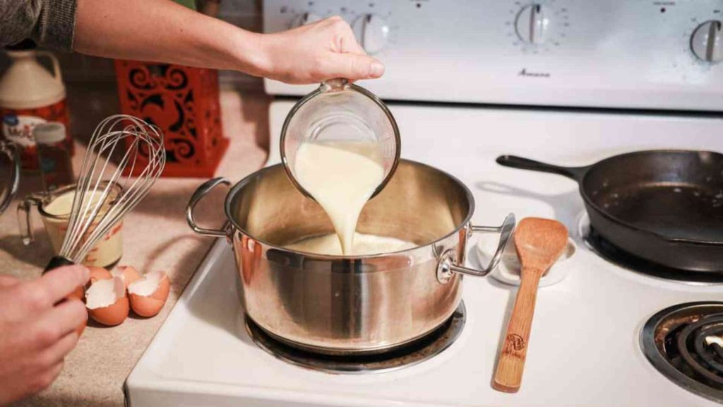 hand pouring milk into a stock pot on the stove