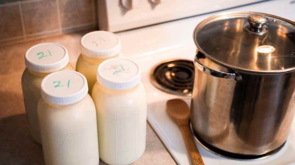 4 half gallon glass jars of raw milk next to a stock pot on a stove
