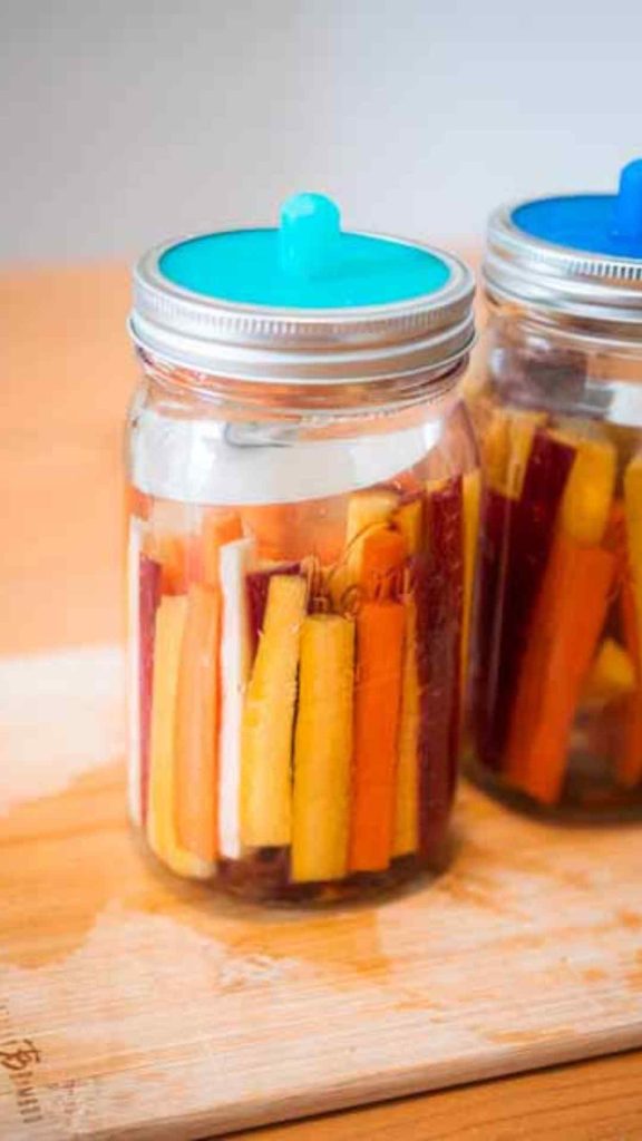 two jars of fermented carrots with blue pickle pipes on top