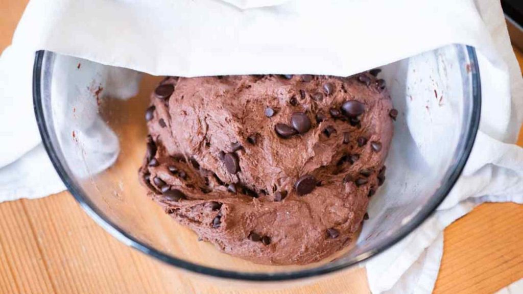 chocolate sourdough bread dough in a glass bowl with a white towel draped across it