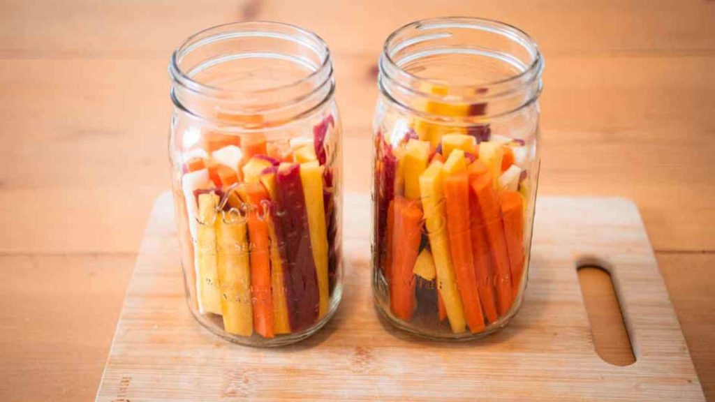 two glass mason jars of sliced rainbow carrots on a cutting board