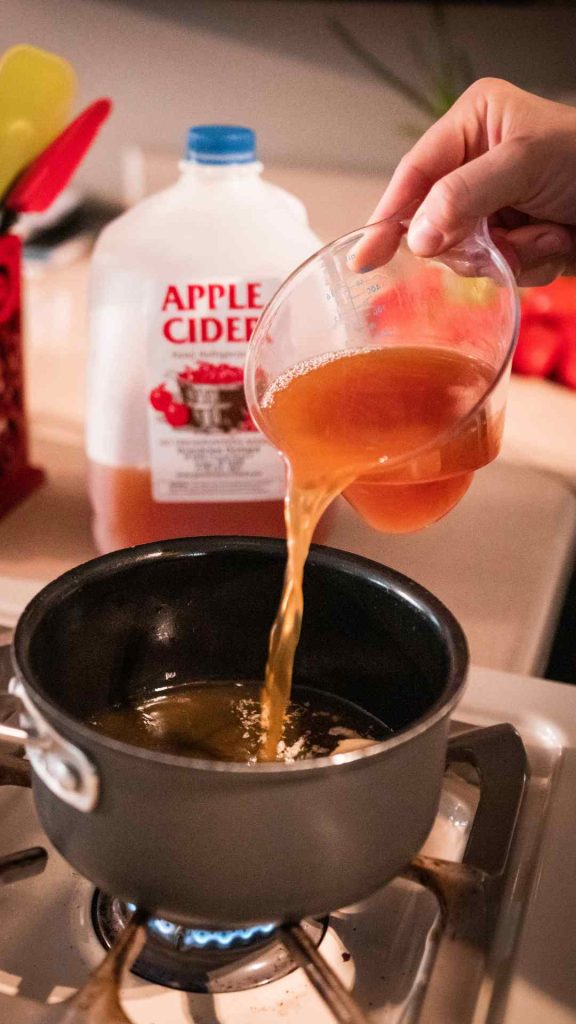 pouring apple cider into a saucepan