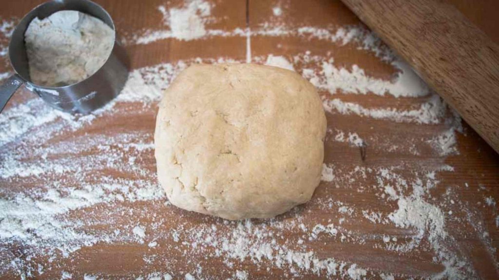 ball of sourdough pie crust on a floured surface with a rolling pin and measuring cup full of flour