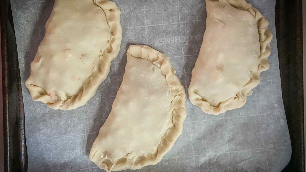 3 traditional yooper pasties on a sheet pan ready to bake