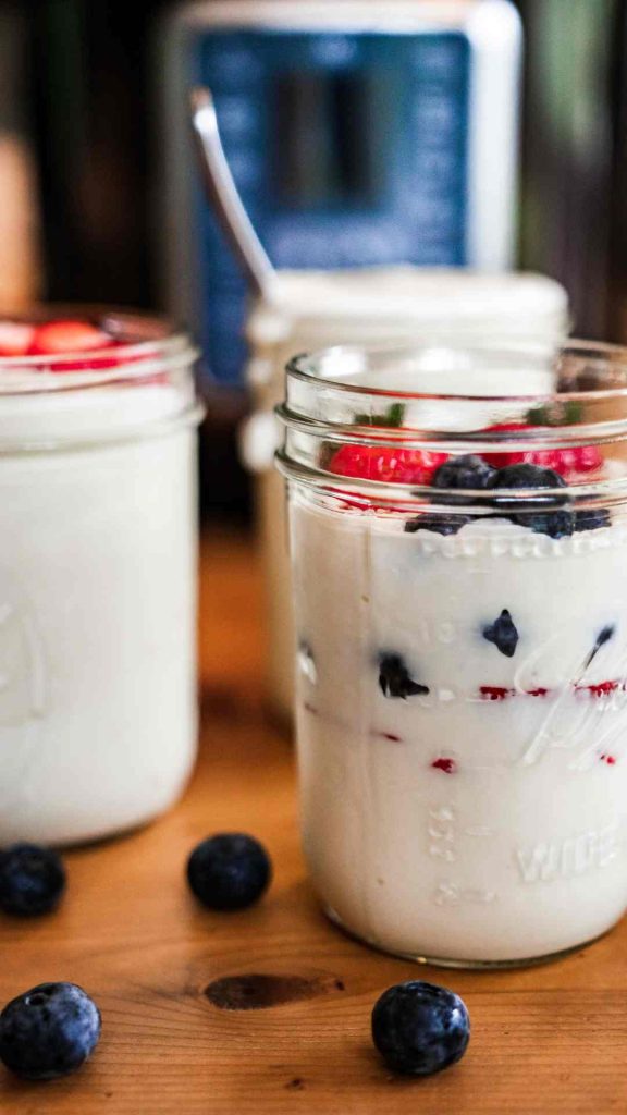 3 jars of raw milk instant pot yogurt with strawberries and blueberries in them. instant pot in the background.