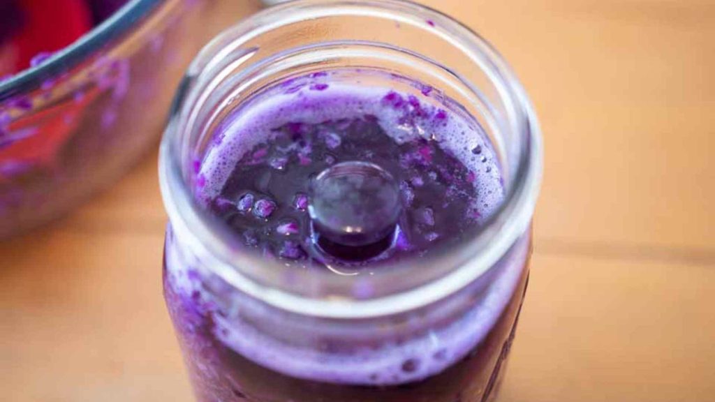 a glass fermentation weight pressed on top of a mason jar of shredded red cabbage sauerkraut, brine rising to the top