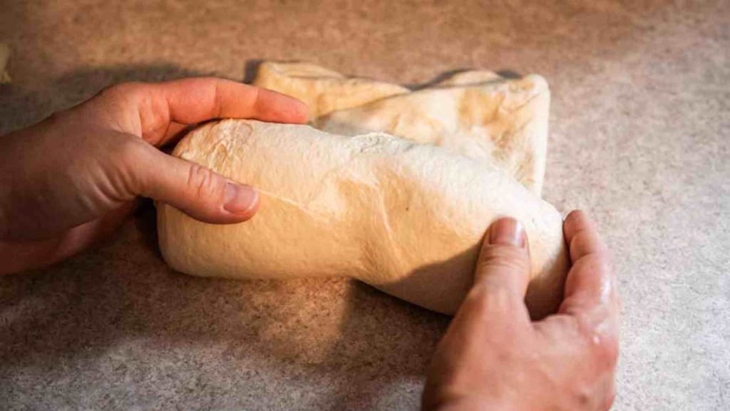 hands rolling up soft sourdough sandwich bread dough for the final rise