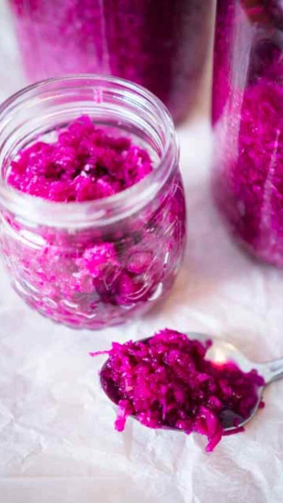fermented red cabbage on a spoon and some more in glass jars in the background