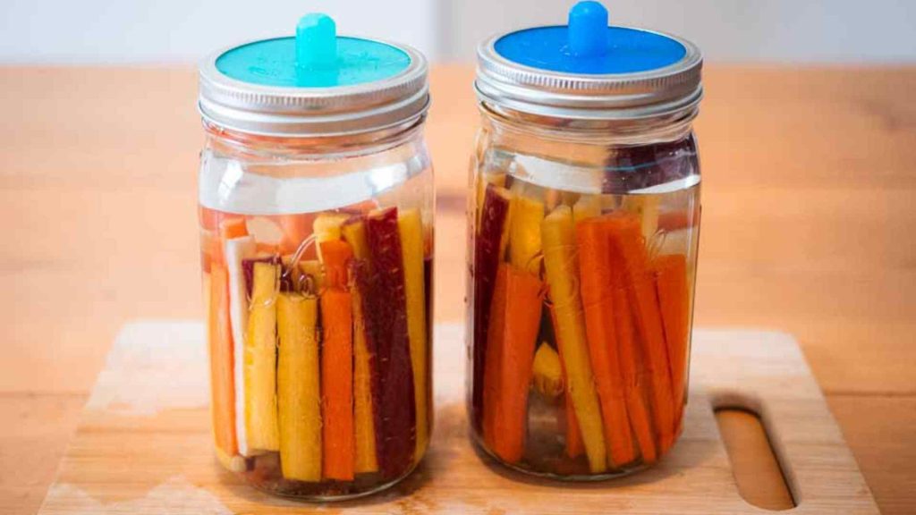 two jars of fermenting carrots with fermentation lids on