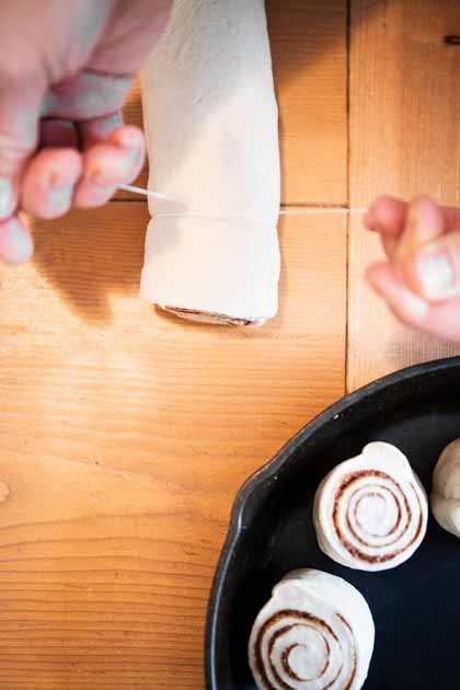 hands using a piece of string to cut the cinnamon roll log into rolls