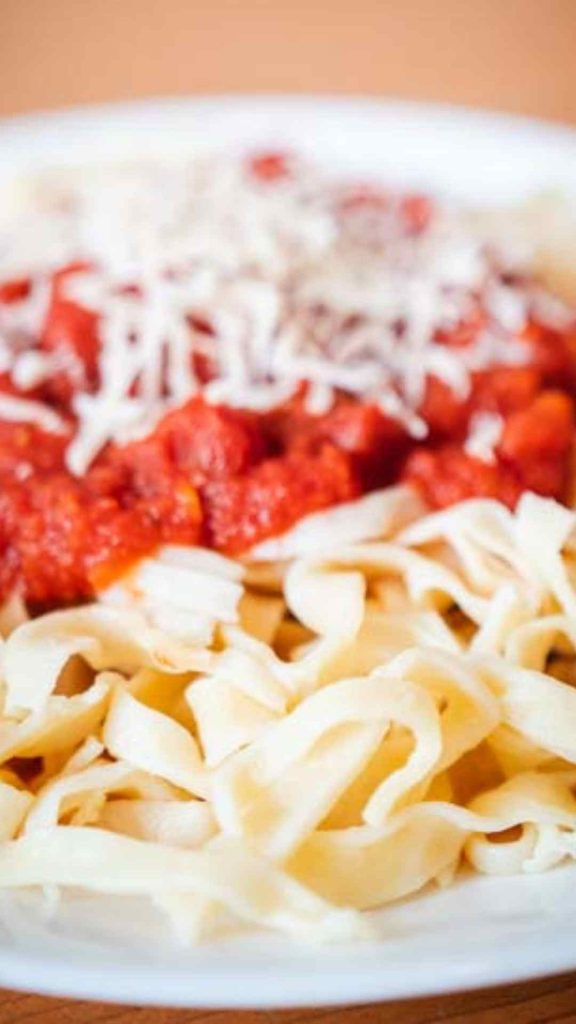 close up of sourdough pasta with marinara sauce and parmesan cheese shredded on top 