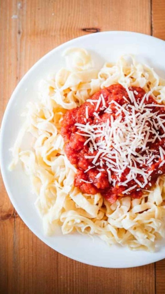 plate of fresh sourdough pasta with marinara sauce and parmesan cheese shredded on top 