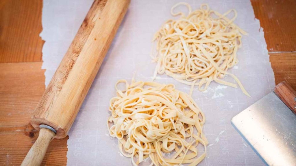 two piles of sourdough pasta noodles with a rolling pin and bench scraper