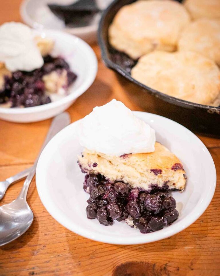 sourdough blueberry cobbler in bowls next to a cast iron of cobbler